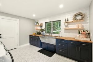 Modern kitchen with black cabinetry, wooden countertops, and natural light from large windows.
