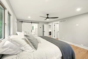 Modern bedroom with white walls, ceiling fan, and cozy bedding.