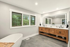 Modern bathroom with freestanding tub and wooden vanity under large mirror.