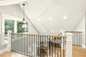 Modern staircase with black metal railing and wooden handrail under sloped ceiling.