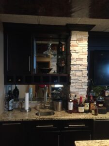 Home bar setup with liquor bottles, glasses, and a stone pillar.