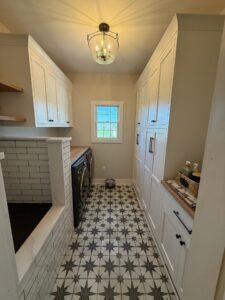 Bright, narrow laundry room with patterned floor tiles and white cabinets.