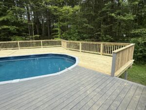 A backyard pool with surrounding wooden deck and railing.