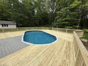 A backyard pool surrounded by a new wooden deck and lush green trees.