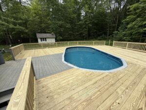 Wooden deck surrounds a blue oval pool in a backyard.