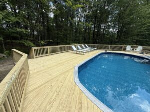 Wooden deck surrounding a blue above-ground pool with lounge chairs and trees around.