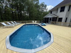 Outdoor pool with wooden deck and lounge chairs beside a house.