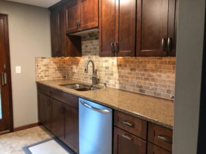 Modern kitchen with wooden cabinets, stone backsplash, and stainless steel dishwasher.