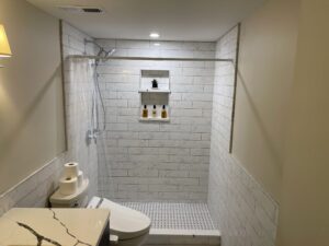 Modern bathroom shower area with white tiles and built-in shelf.