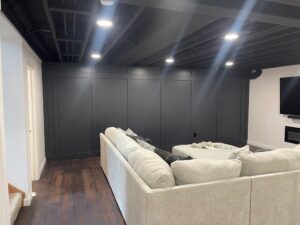 Modern living room with a large beige sectional sofa and dark paneled wall.