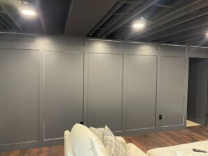 A gray paneled wall with recessed lighting above and a white couch in the foreground.