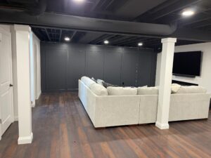 A spacious basement with a large beige sectional sofa and dark wooden floors.