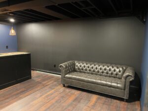 A dark gray Chesterfield sofa against a gray wall in a dimly lit room.