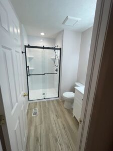 Modern bathroom with glass shower door and wood-like flooring.